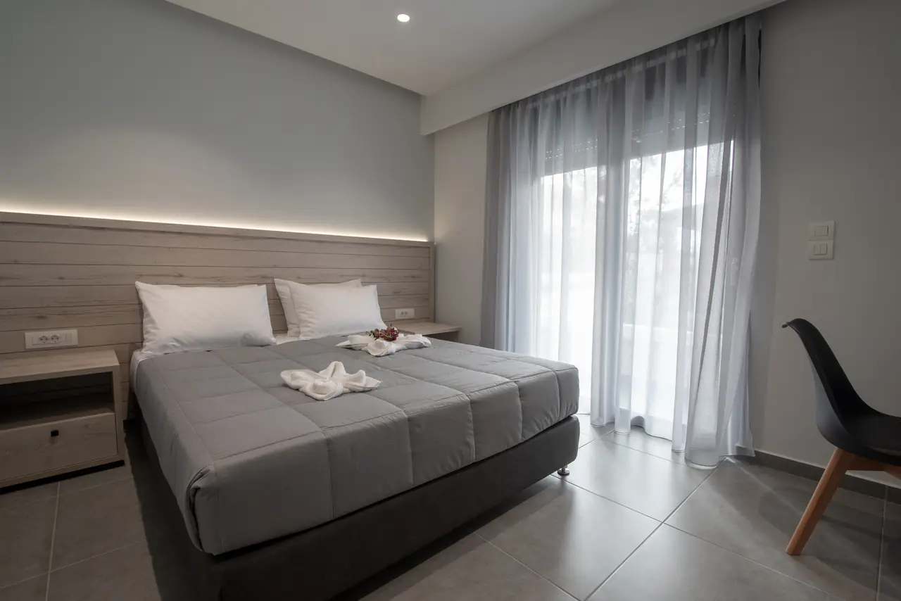 Double bed with folded towel swans next to sheer curtains