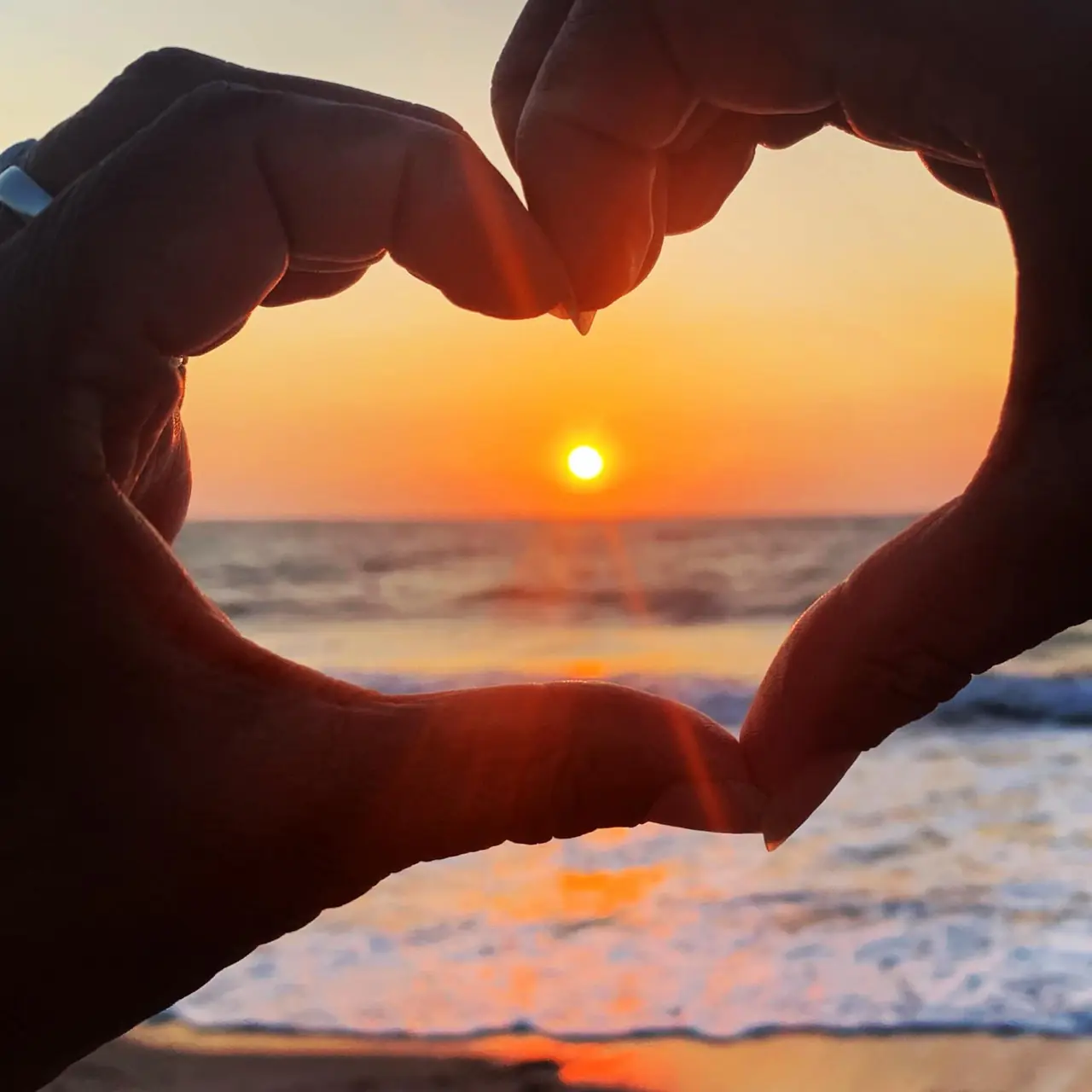 Hands forming a heart around the sunset